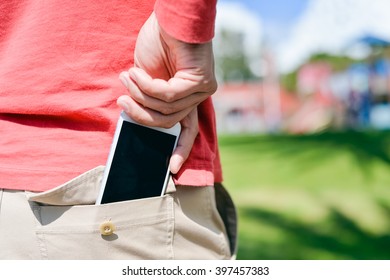 Closeup on man hand holding taking a smartphone in the back pocket on sunny background outdoors 