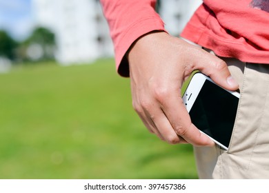 Closeup on man hand holding taking a smartphone in the pocket on sunny background outdoors 