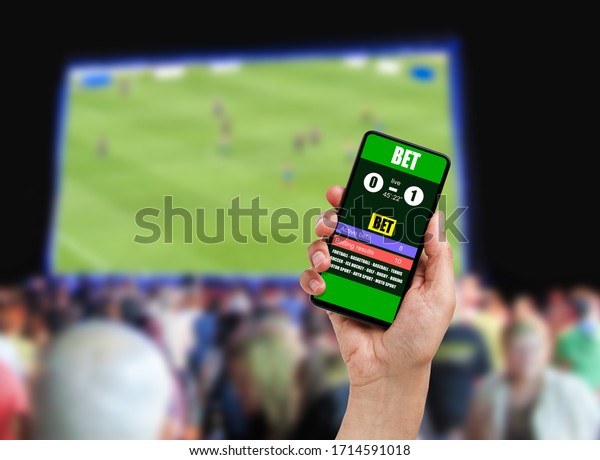 Close-up on man holding a cell\
phone while winning an online bet on a football game at\
bar.