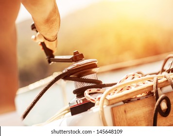 Closeup on man holding crank on the yacht, body part, bright yellow sunset, sailboat detail, active lifestyle, yachting sport, summer relaxation concept