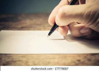 Closeup on a man's hand writing on apiece of paper with a pen