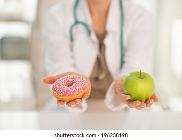 Closeup on medical doctor woman giving a choice between apple and donut