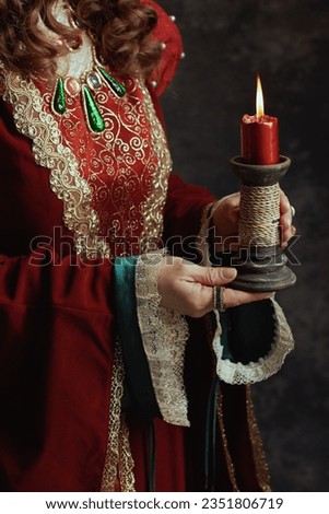 Closeup on medieval queen in red dress with candle.