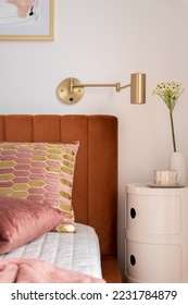 Close-up on modern beside table with stylish decorations and cozy and elegant bed with velvet headboard and nice pillows