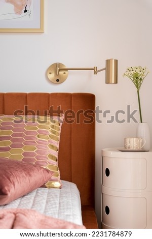 Close-up on modern beside table with stylish decorations and cozy and elegant bed with velvet headboard and nice pillows