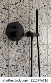 Close-up on modern, black shower head in bathroom with square, terrazzo style wall tiles