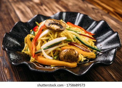 Closeup on mushrooms and vegetables udon wok noodles in a black plate on the wooden table, horizontal - Shutterstock ID 1758689573