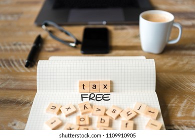 Closeup on notebook over vintage desk surface, front focus on wooden blocks with letters making Tax Free text. Business concept image with office tools and coffee cup in background