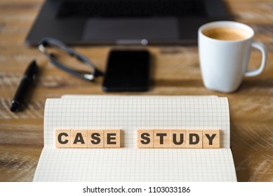 Closeup on notebook over wood table background, focus on wooden blocks with letters making Case Study text. Concept image. Laptop, glasses, pen and mobile phone in defocused background