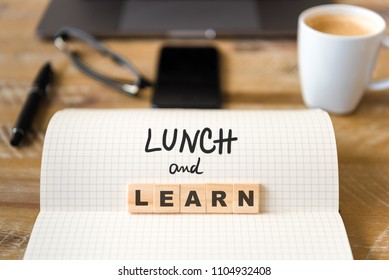 Closeup On Notebook Over Wood Table Background, Focus On Wooden Blocks With Letters Making Lunch And Learn Text. Concept Image. Laptop, Glasses, Pen And Mobile Phone In Defocused Background