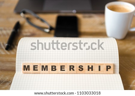 Closeup on notebook over wood table background, focus on wooden blocks with letters making Membership text. Concept image. Laptop, glasses, pen and mobile phone in defocused background