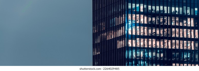 Close-up on an office building in the evening with some lightened workspaces against dart night sky. Modern, glazed skyscraper. Financial district. Late hours in the office. - Powered by Shutterstock