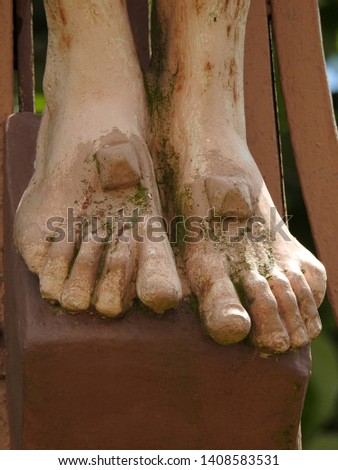 Closeup on one of the Five Holy Wounds (stigmata) of Jesus Christ as large nails go through feet covered with moss of an outdoor statue of the crucifixion in southwestern France, Occitanie
