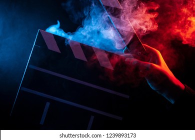 Close-up on an open clapperboard in hand before starting shooting a film with multi-colored smoke around with red and blue backlighting on a black isolated background - Powered by Shutterstock