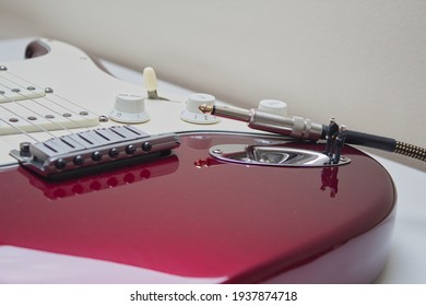 Close-up On Part Of An Electric Red Guitar Where 2 Older Men As Miniature Figures Stand Next To The Cable Plug And Talk. Light Background