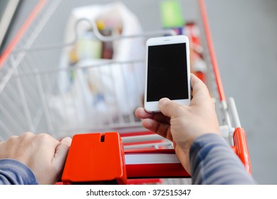 Closeup On Person Holding Mobile Phone In Hand During Shopping. Cart On Store Background