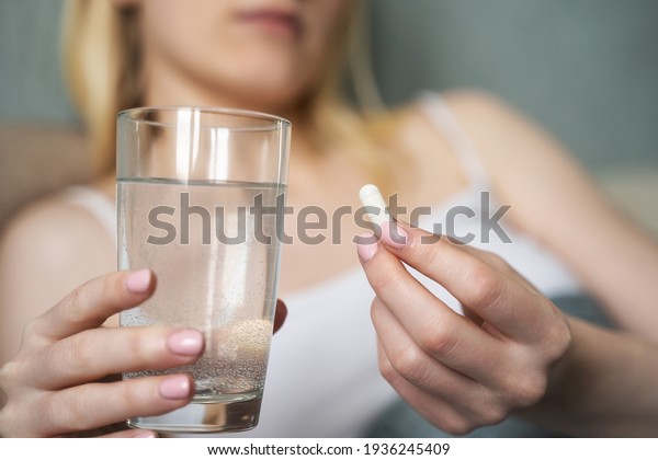 Closeup on pills pack in hand of ill young woman\
laying on sofa.