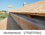 A close-up on plywood board, OSB used for roof sheathing installed on roof beams with blurred roofing construction in the background.