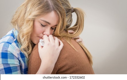 Closeup On Sad Teen Daughter Crying By Problems In The Shoulder Of Her Mother. Mother Embracing And Consoling Daughter.