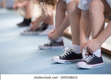 Close-up On School Kids' Legs While They're Sitting On A Bench And Tying Their Sport Shoes For Physical Education Activities