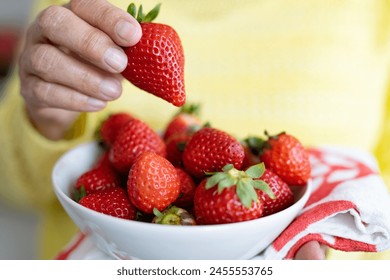 Close-up on senior woman's hand holding a bowl of red fresh ripe strawberries. Healthy eating concept
