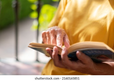 Closeup on senior woman's hands in yellow shirt resting in public park reading a book, caucasian female enjoying retirement and free time - Shutterstock ID 2160165851