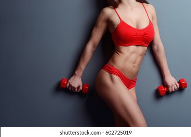 Closeup on sexy toned body with visible abdominal muscles. Dressed in red bra and thongs woman holding little dumbbells.