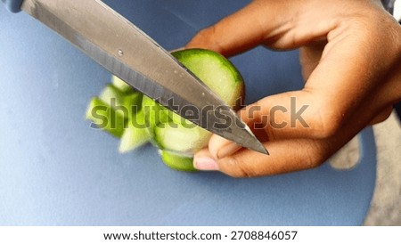 A close-up on the sharp knife blade as it expertly slices a fresh green cucumber. Focused on food prep precision on the blue cutting board