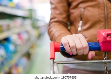 Closeup On Shopper Woman Hands On Supermarket Trolley Carries With Shopping Mall Display Shelf On The Background