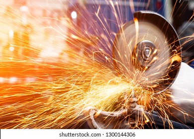 Close-up on the sides fly bright sparks from the angle grinder machine. A young male welder in a white working gloves grinds a metal product with angle grinder in the garage