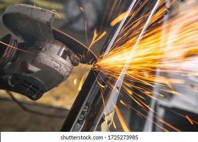 Close-up on the sides fly bright sparks from the angle grinder machine. A young male welder  grinds a metal product with angle grinder in the garage - Powered by Shutterstock