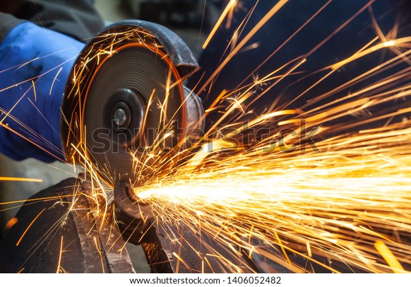 Close-up on the sides\
fly bright sparks from the angle grinder machine. A young male\
welder in a white working gloves grinds a metal product with angle\
grinder in the garage