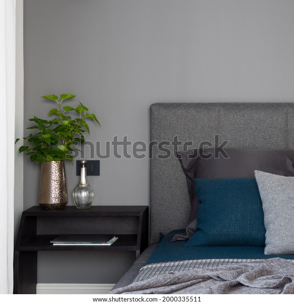Close-up on simple, black\
nightstand with decorations next to comfortable bed with stylish\
bedclothes