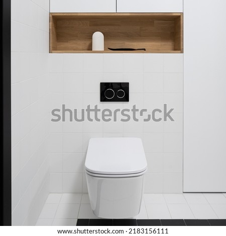 Close-up on simple white toilet in lavatory with black and white floor and wall tiles and wooden shelf