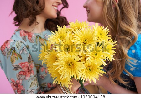 Closeup on smiling mother and child with long wavy hair with yellow chrysanthemums flowers isolated on pink.