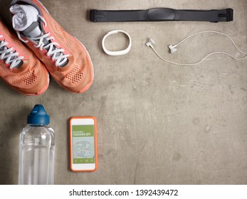 Closeup on sneakers, heart rate monitor, bottle of water, white fitness tracker, headphones, smartphone with gps activity tracking app laying on the floor.