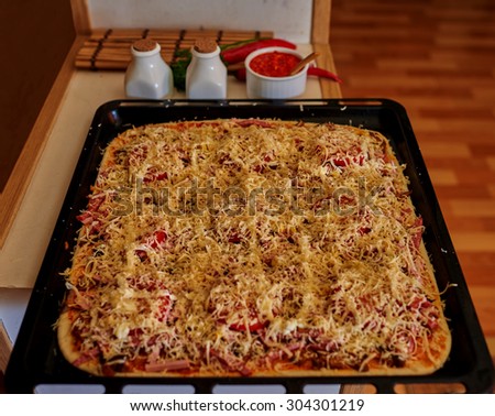 Close-up on the table is a baking homemade pizza with minced meat and pepperoni and various types of cheese
