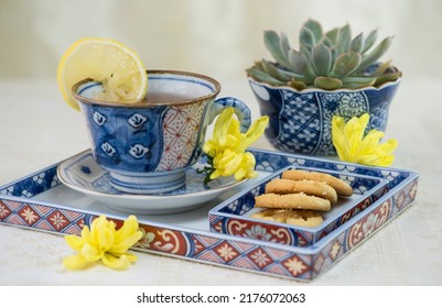 Closeup on tea time table display. Chrysanthemsum lemon tea and cookies in blue theme chinaware complement with rosettes succulent plant. Lacy cream white color table cloth and background.
