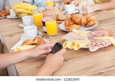 Close-up On Teenager Texting On Her Mobile Phone In The Kitchen While The Rest Of The Family Enjoy Breakfast