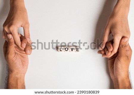 Closeup on two young lovers holding hands isolated on white background, "Love" written with dice