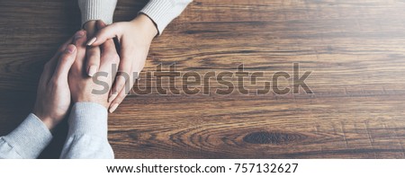 Closeup on two young lovers holding hands at a table