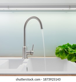 Close-up on white kitchen sink with simple silver kitchen faucet turned on