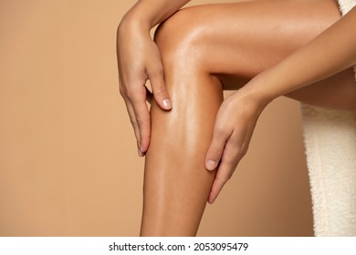 Close-up on a woman applying cream on her legs on beige background