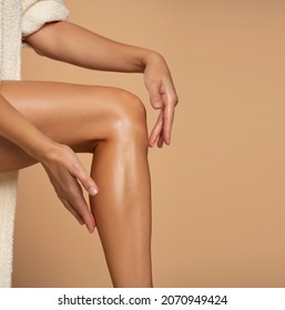 Close-up on a woman applying cream on her legs on beige background
