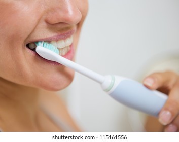 Closeup on woman brushing teeth with electric toothbrush