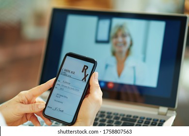 Closeup on woman with electronic rx on a smartphone and doctor on video call on a laptop in background in the house in sunny day.