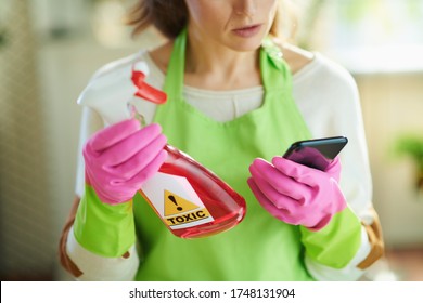 Closeup On Woman In Green Apron And Pink Rubber Gloves In The Living Room In Sunny Day Reading About Cleaning Product On Internet Using Smartphone.