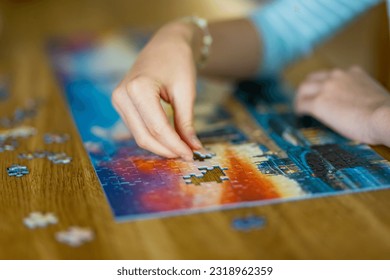 Close-up on woman hand playing puzzles at home. Connecting jigsaw puzzle pieces in a living room table, assembling a jigsaw puzzle. Fun family leisure. - Powered by Shutterstock