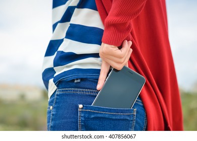 Closeup on woman hand takes out smartphone of her rear pocket of jeans on outdoors background