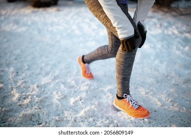 Closeup On Woman In White Jacket Having Leg Pain Outdoors In The City Park In Winter.